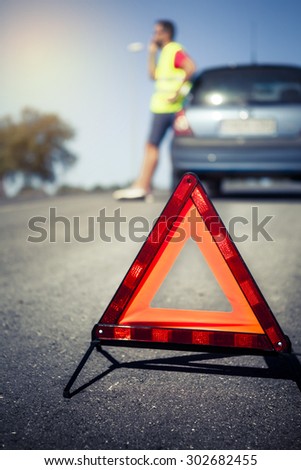 Emergency triangle on the road. Stopped car and man calling by phone in the background.