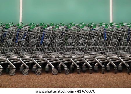 A long row of shopping trolleys / carts, outside of a large supermarket.