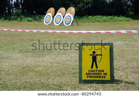 Caution: Archery in Progress sign, with archery targets in the background