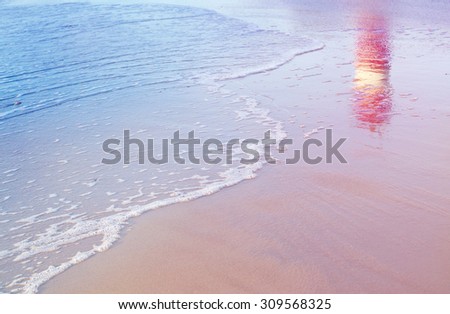 lighthouse reflection among sea waves on beach sand