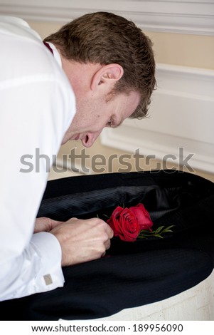 Getting ready. A handsome groom is trying his best to fit his rose to his jacket.