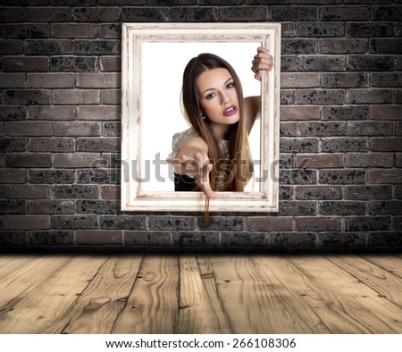Abstract image of a beautiful woman trapped in a picture frame over a brick wall background.
