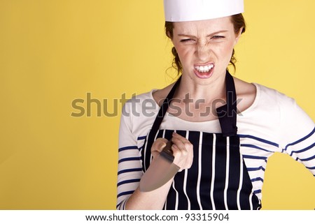 A young and angry female chef pointing a chef’s knife on a yellow background. Angry female chef.