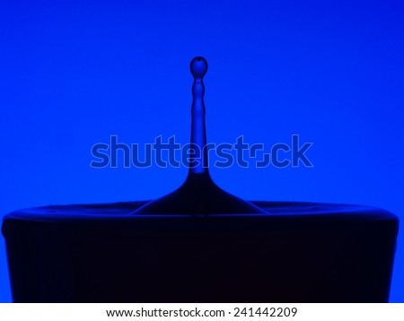Water drop backlit macro. Pillar of water rises out of calm container..
