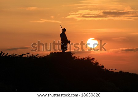 Lone bagpiper at sunset playing a sad tune