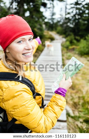 Happy woman hiking and reading map in forest, hiker with dog, Karkonosze Mountains in Poland. Young female backpacker walking with canine. Trekking and travel in wilderness.