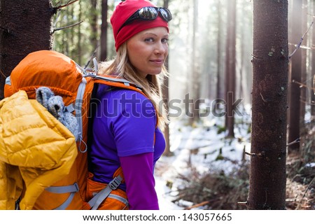 Woman hiking in white winter forest. Recreation and healthy lifestyle outdoors in nature. Beauty blond looking at camera on sunset.