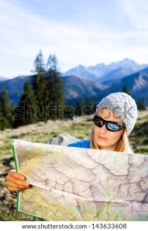 Young woman hiker reading map in mountains on hiking trip. Female trekker camping and planning in autumn nature, outdoors activity, navigation and lost concept