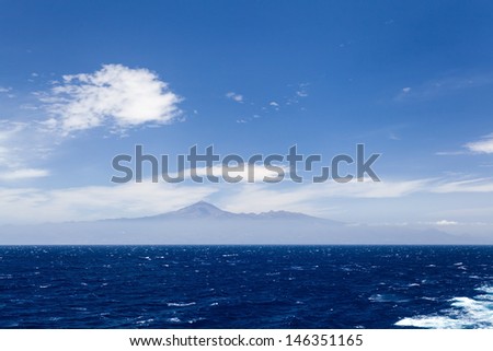 Ocean, sky and Tenerife island with El Teide mountain. Canary Islands on the blue ocean over cloudy beautiful sky. Vacations or holidays in Spain, Europe.