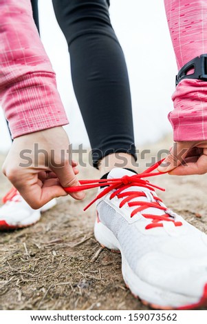 Woman runner tying sport shoes. Walking or running legs, autumn adventure and exercising outdoors. Young female hiker ready to hike. Motivation and inspiration fitness concept outside nature.