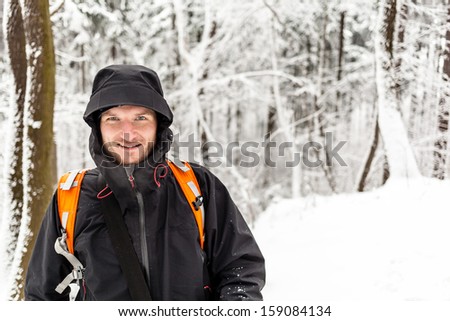 Man hiker hiking in white winter forest with backpack. Recreation and healthy lifestyle outdoors in snowy nature. Young male looking at camera and smiling.