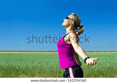 Young female runner exercising and stretching in summer nature. Happy woman running on country road, bright sunlight and colorful environment, sport and fitness