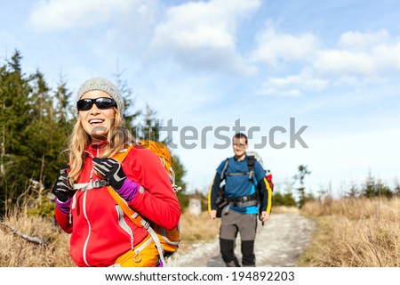 Man and woman hikers hiking on mountain trail autumn or winter nature. Young couple backpackers walking in forest landscape. Happy trekkers on travel trip with backpacks, camping outdoors.