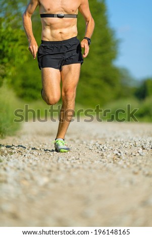 Man runner running on country road in summer sunset. Young athlete male training and doing workout outdoors in nature. Checking pulse trace heartbeat using gps watch