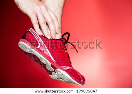 Physical running injury and leg ankle pain, sport shoes and hand massage over red background