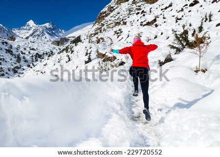 Woman running on white snow in Himalaya Mountains in Nepal. Motivation and inspiration fitness activity. Adventure cross country runner on snow trail in beautiful mountain landscape.