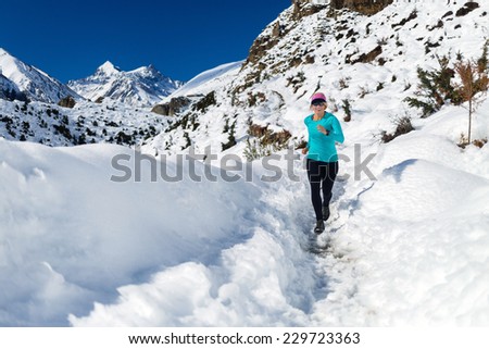 Woman running on white snow in Himalaya Mountains in Nepal. Adventure cross country runner on snow trail in beautiful mountain landscape.