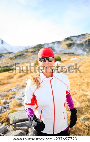 Happy young woman running in mountains on winter fall sunny day, motivation and inspiration fitness contept landscape. Active runner or hiker power walking outdoors in nature, sunset.