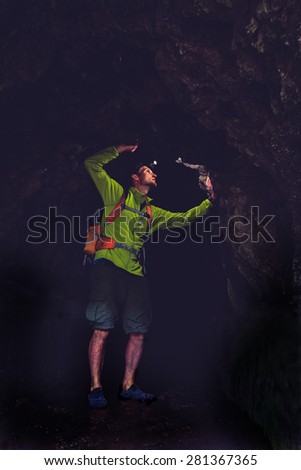 Man walking and exploring dark cave tunnel with light headlamp underground. Mysterious deep dark, explorer discovering looking on rock wall inside.