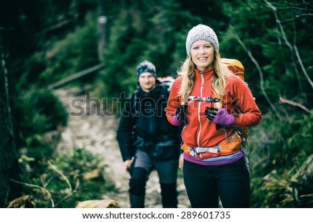 Man and woman happy couple hikers trekking in green autumn forest and mountains. Young people walking on trail with backpacks, healthy lifestyle adventure, camping on hiking trip, vintage photo style.
