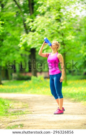 Woman runner running and drinking sports drink water in park when working out and training, healthy lifestyle, exercising on bright summer trail