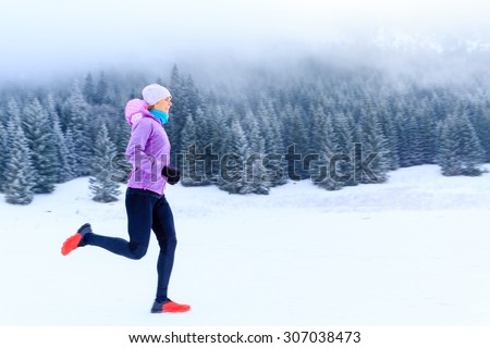 Sport, fitness inspiration and motivation. Young happy woman cross country running in mountains on snow, winter day. Female trail runner jogging exercising outdoors.