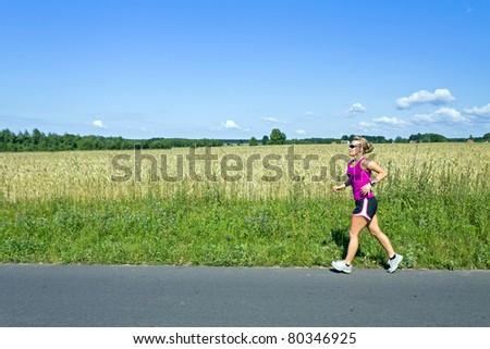 Woman running on country road over blue sky and landscape and meadow
