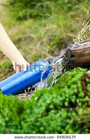Woman filling water bottle from stream on hiking trip, summer activity