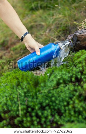 Woman filling water bottle from spring on hiking trip