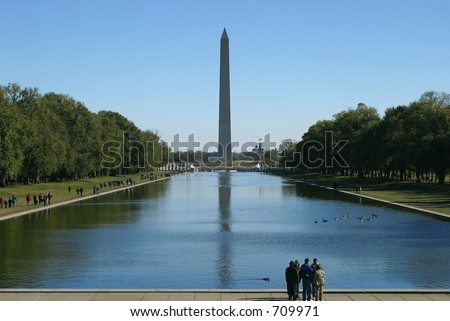 A small group of people standing at the reflecting pool across from the Washington Monument.