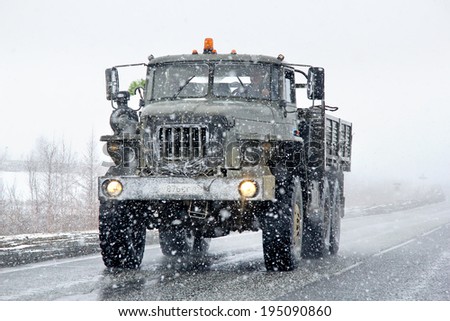 NOVYY URENGOY, RUSSIA - MAY 23, 2014: Green Ural 4320 flatbed off-road truck at the interurban road during a heavy snowfall.