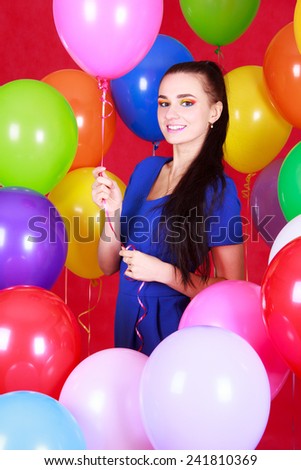Portrait of a young attractive woman among many bright balloons over red background