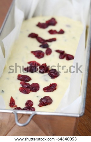 Cake tin with zucchini bread batter and dried cranberries ready to be put into the oven. Shallow dof