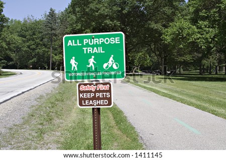 Signs posted along an all purpose, walking, jogging riding, bicyle path in a public park along roadway.