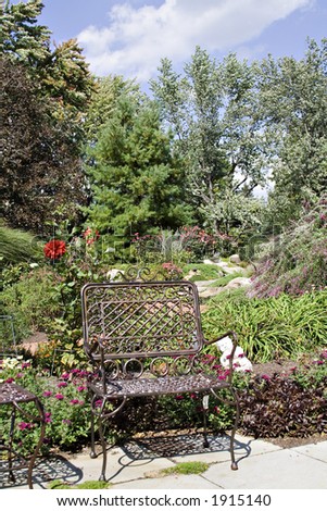 A beautiful garden - bench, paths, flowers, trees, sky.