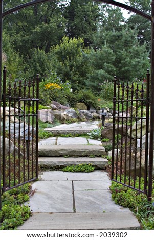 The  black wrought-iron garden gate entrance to an enchanted, peaceful flower garden.