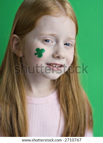 A very young red-haired girl with green shamrock painted on her face for St. Patrick's Day.