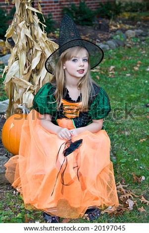 A small blond girl dressed in a fall Halloween witch costume.