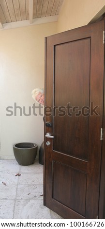 Senior woman peeping round door with copy space