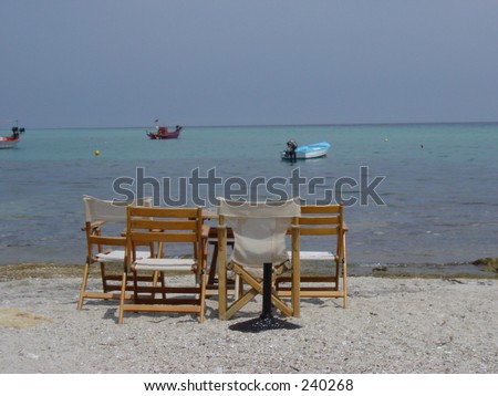 Resort Sun chairs round table on beach looking at speed boats,Sun Sand and Sea. Copy space in sky.