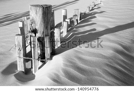 Wooden fence in sand dunes with strong shadows from sunlight