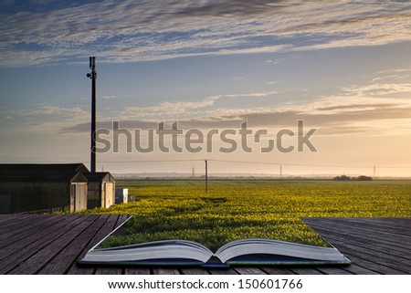 Creative concept pages of book Landscape of farm buildings being lit by rising sun over rapeseed crop field