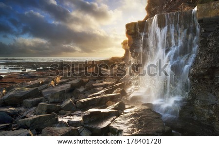 Beautiful landscape waterfall flowing into rocks on beach at sunset