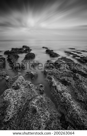 Black and white landscape looking out to sea with rocky coastline and beautiful sunset sky