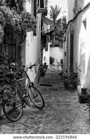 Mediterranean alley way between old houses and buildings with bike and local residents  black and white