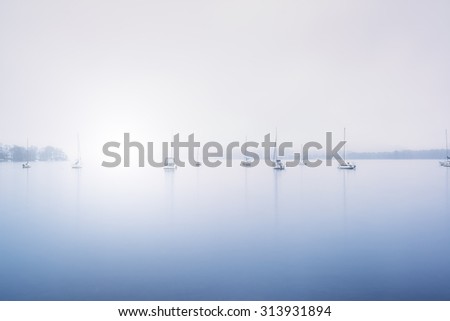 Sailing boats in fog on Lake Windermere in Lake District toned blue