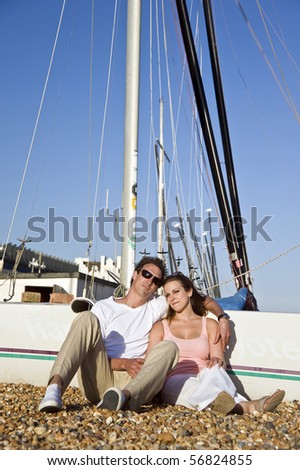 Young attractive couple relaxing on beach with boats in background