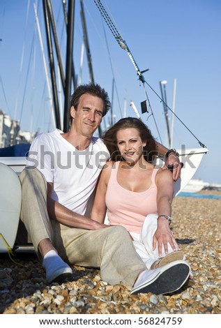 Young attractive couple relaxing on beach with boats in background