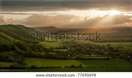Lovely landscape of countryside hills and valleys with setting sun lighting up side of hills whit sun beams through dramatic clouds