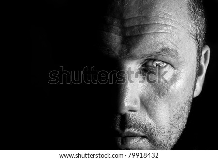 Unusual portrait of male face half hidden in shadows with visible eye pupil replaced by man\'s distorted face